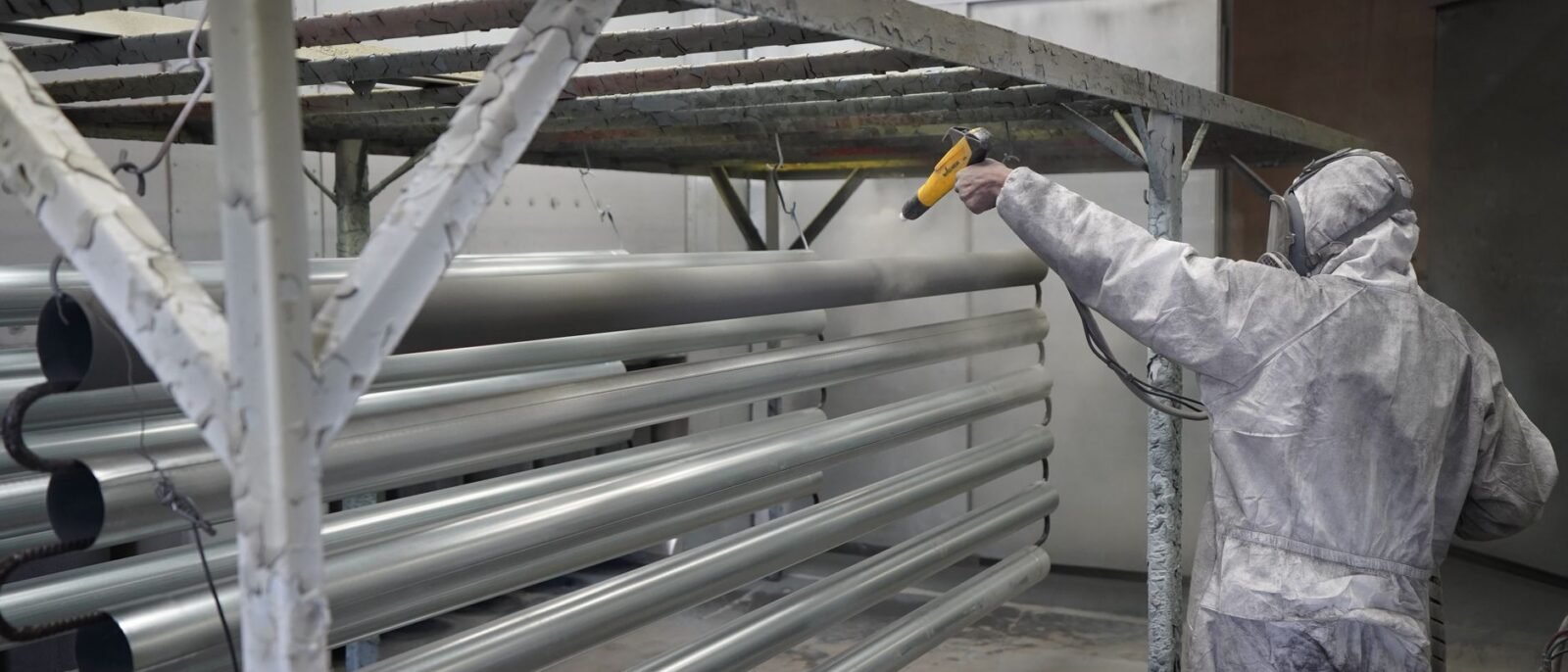 Técnico aplicando tinta em pó em tubos de metal em um ambiente de oficina