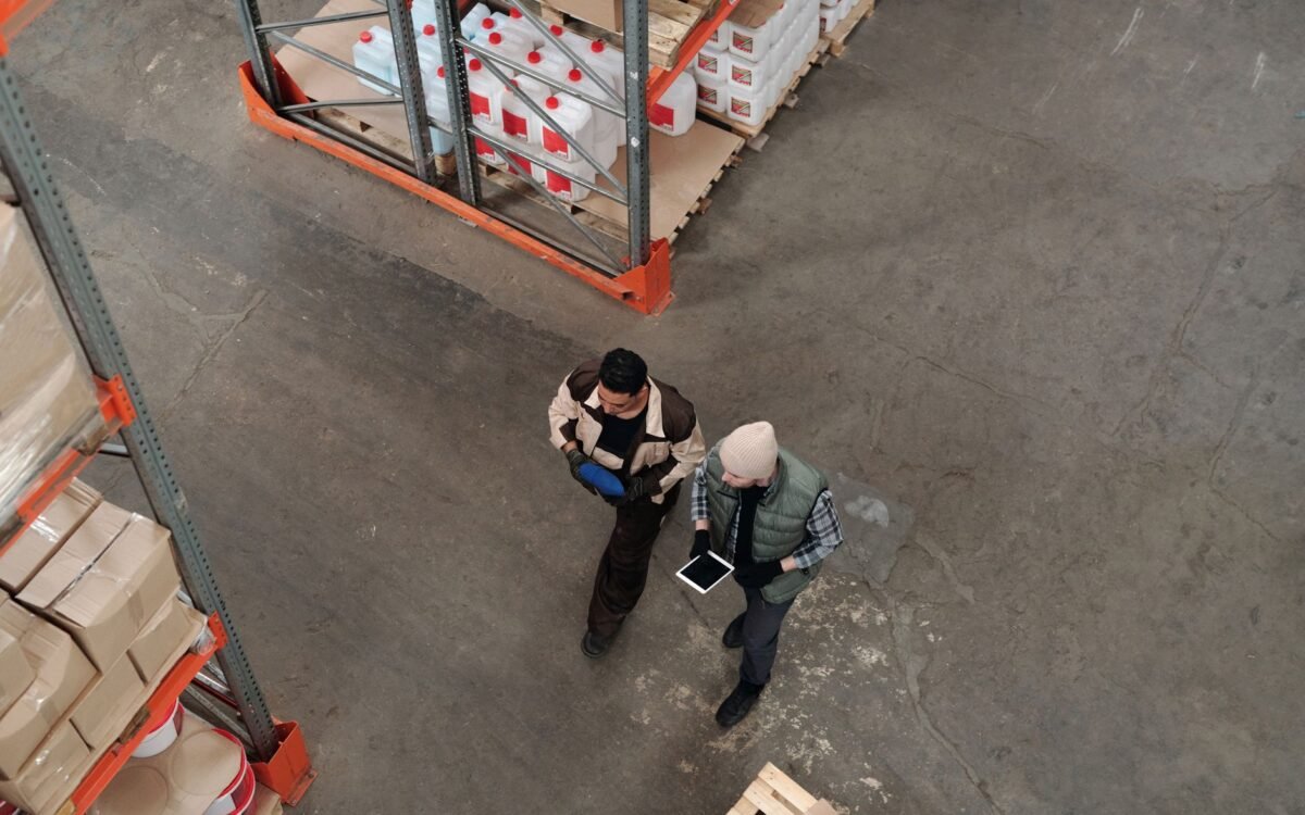 Dois trabalhadores discutindo inventário em um armazém, usando um tablet digital para coordenação