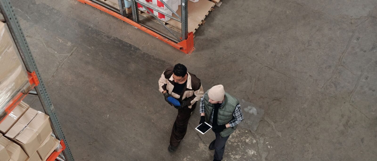 Dois trabalhadores discutindo inventário em um armazém, usando um tablet digital para coordenação